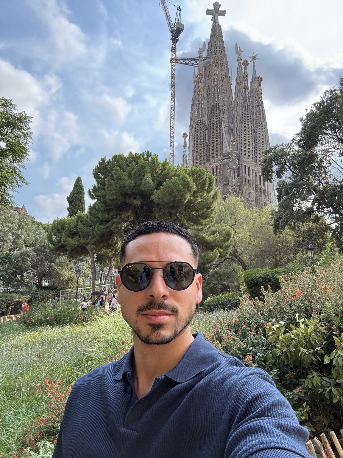 Joel Figueroa con polo azul marino y gafas de sol, con jardines y la Sagrada Familia al fondo